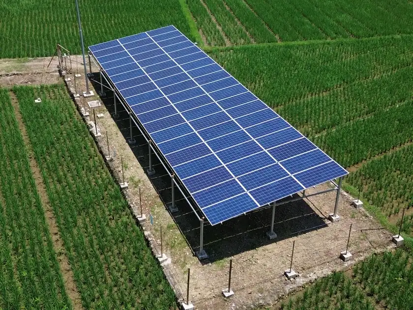 Foto drone deretan panel surya di atas rangka besi untuk pompa irigasi di tengah sawah